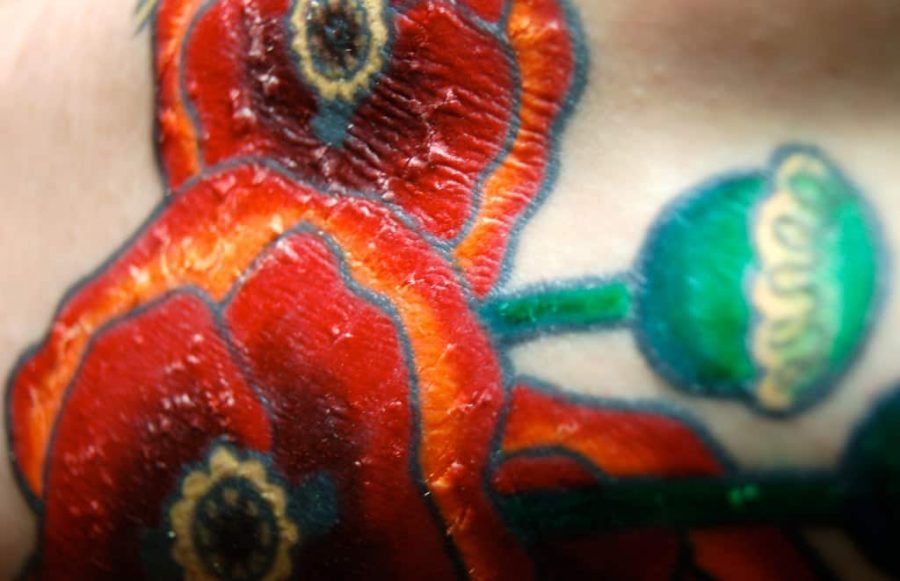 Close-up of a healing tattoo with scabbing and shiny skin, featuring vibrant red poppy flowers with green stems and buds
