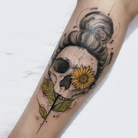 Artistic tattoo featuring a skull with a messy bun hairstyle, a vibrant sunflower over one eye, and leafy details, designed in a watercolor style.