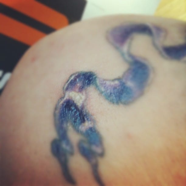 Close-up of a healing tattoo with scabbing and fading ink, featuring a wavy blue and purple design