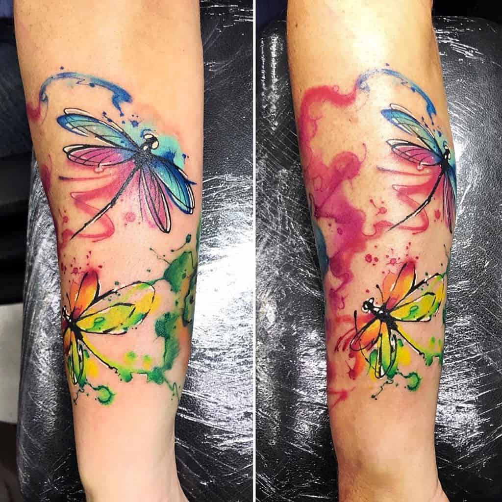 Vibrant watercolor dragonfly tattoo on the forearm, featuring bold splashes of blue, pink, green, and yellow for an artistic look.