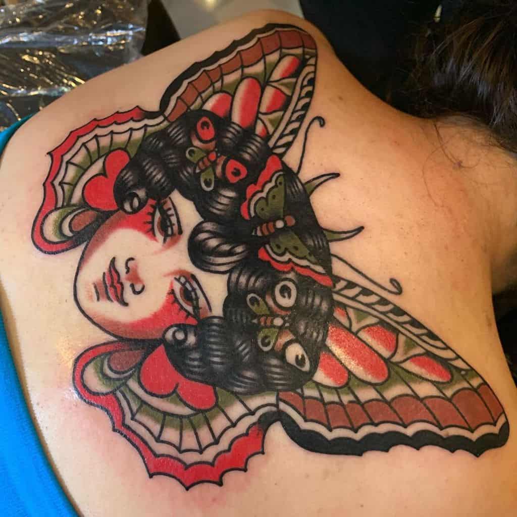 Bold and colorful neo-traditional tattoo of a woman's face blended with butterfly wings, creating a striking and artistic back piece.