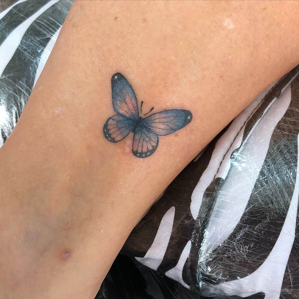 Delicate blue and pink butterfly tattoo on the leg, featuring soft shading and fine details for a subtle and elegant design.
