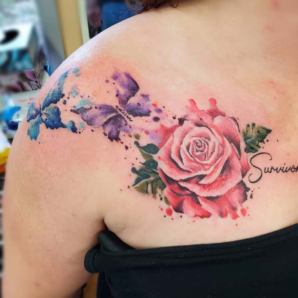 Watercolor-style tattoo on the shoulder featuring blue and purple butterflies blending into a vibrant pink rose with the word 'Survivor'.