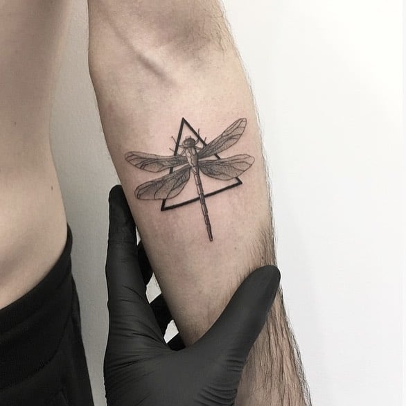 Minimalist dragonfly tattoo on the inner forearm, featuring fine linework and a geometric triangle for a modern, clean design.