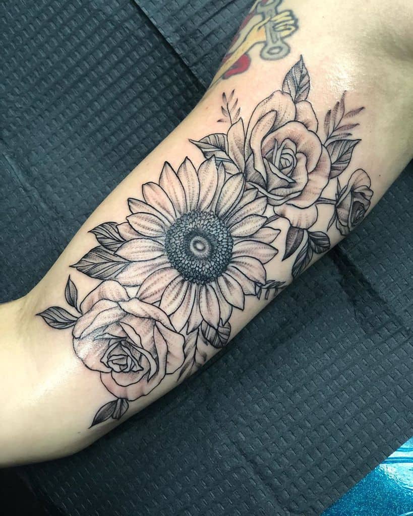 Black and grey forearm tattoo featuring a detailed sunflower surrounded by roses, with fine linework and soft shading for depth.