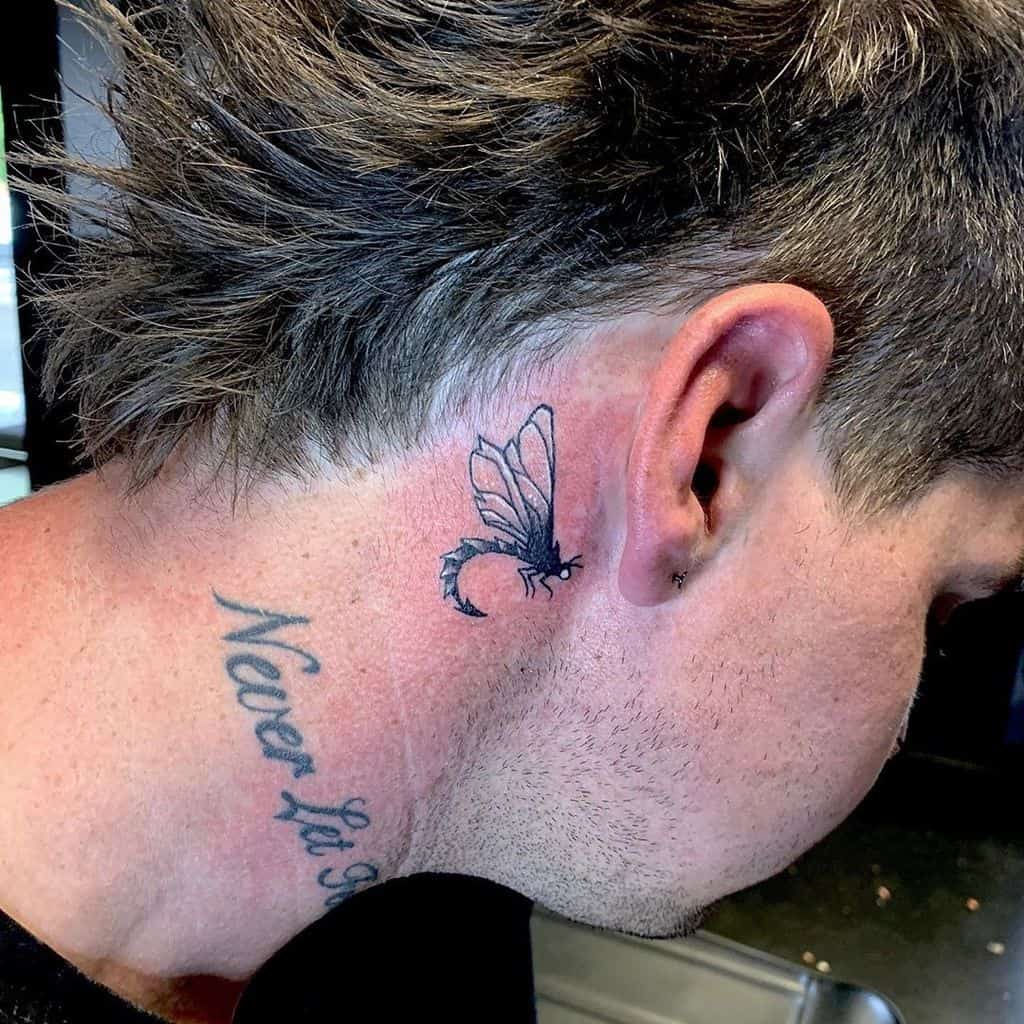 Small dragonfly tattoo behind the ear with a unique, curved tail. The fine line design adds a subtle and edgy touch.
