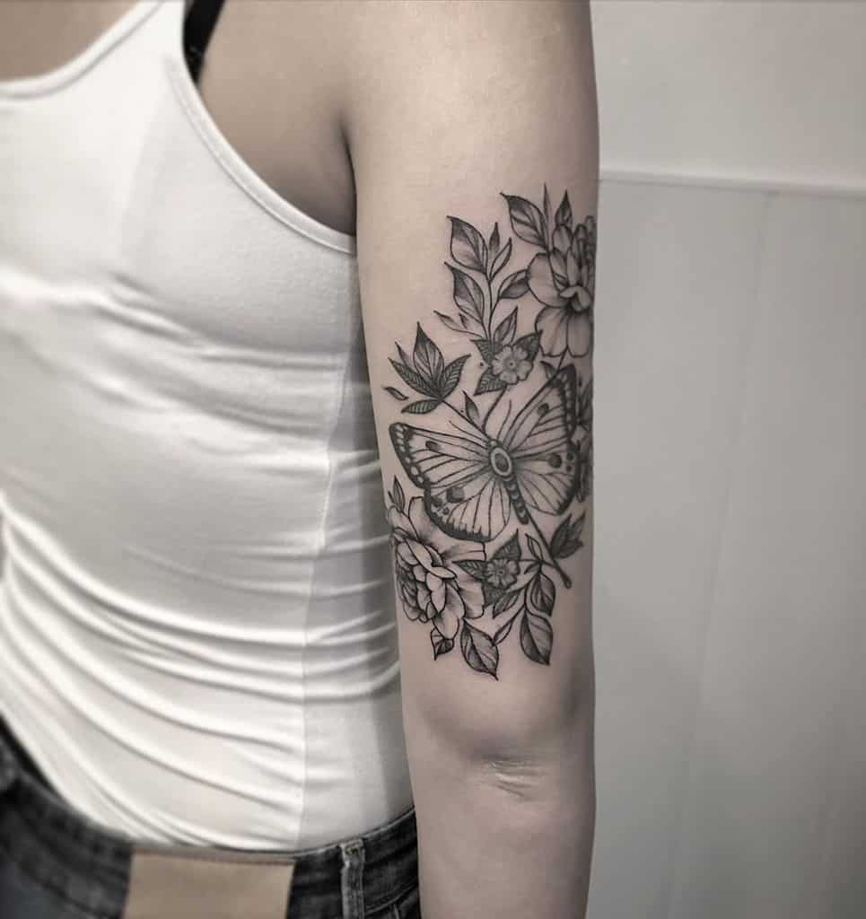Elegant black and grey butterfly and floral tattoo on the upper arm, featuring delicate shading and intricate botanical details.