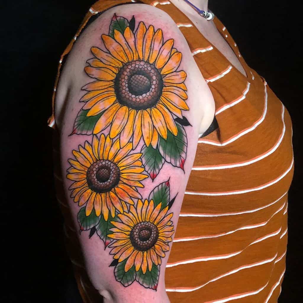Bright and colorful sunflower tattoo sleeve covering the upper arm, featuring three large sunflowers with bold yellow petals and green leaves.