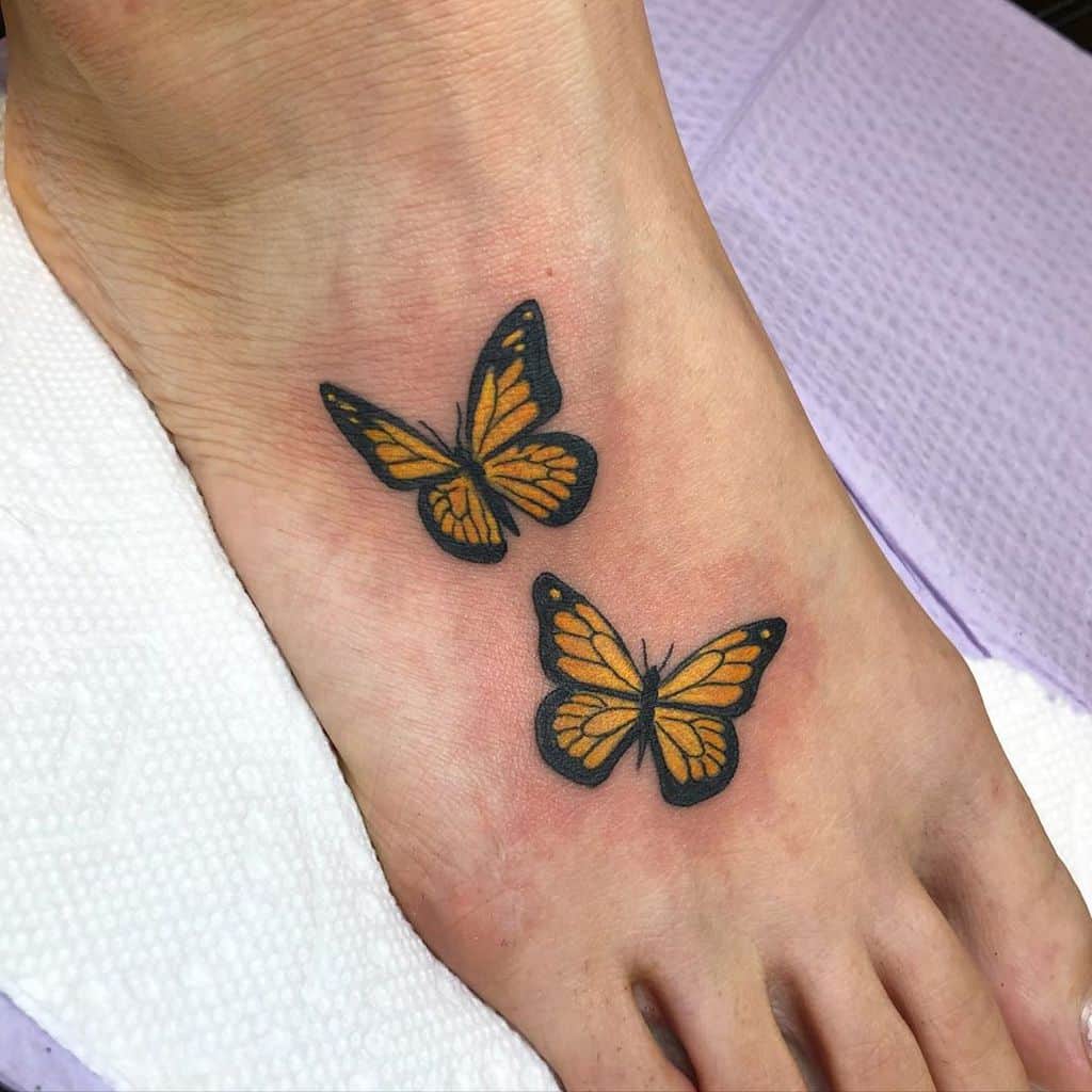 Delicate twin monarch butterfly tattoos on the foot, symbolizing freedom, transformation, and a graceful connection to nature.