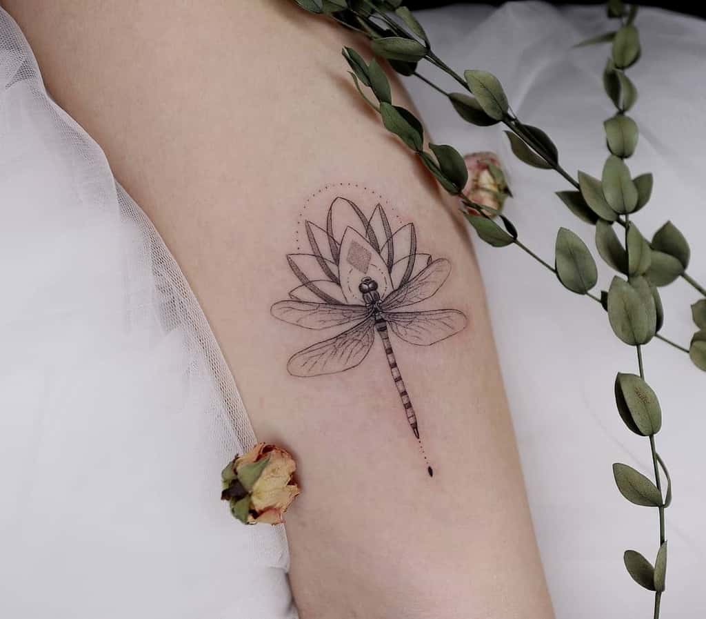 Delicate dragonfly and lotus tattoo with fine linework, subtle dot shading, and geometric accents for an elegant, nature-inspired design.