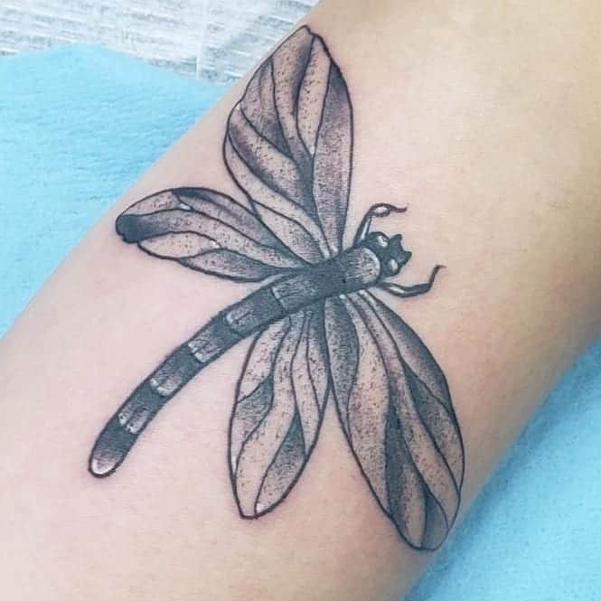 Black and grey dragonfly tattoo with fine shading and bold outlines. The intricate wing details add depth and realism to the design.