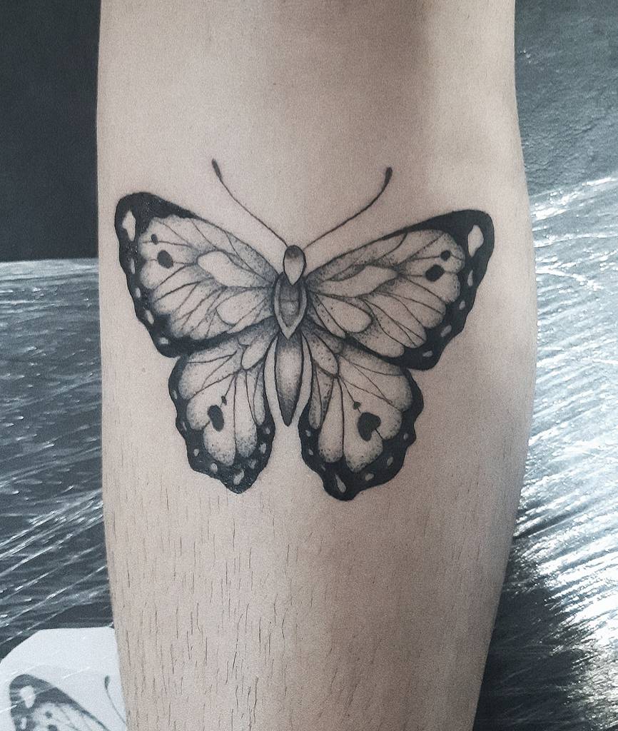 Black and gray butterfly tattoo on the leg, featuring intricate shading, fine line details, and a realistic wing pattern.