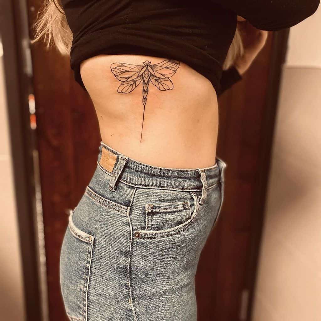 Elegant black ink dragonfly tattoo on the ribcage, featuring fine linework and geometric details for a minimalist look.