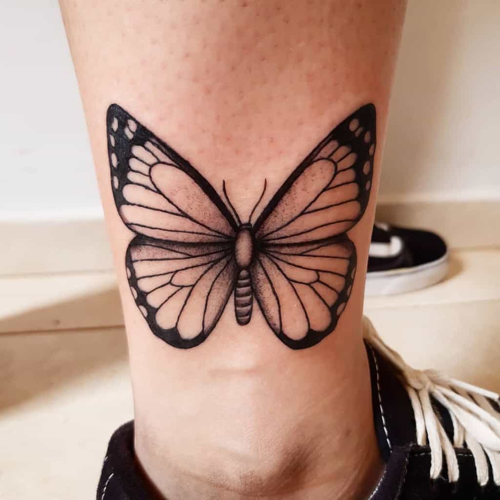 Realistic black and grey butterfly tattoo on the ankle with delicate shading and fine details for an elegant and timeless look.