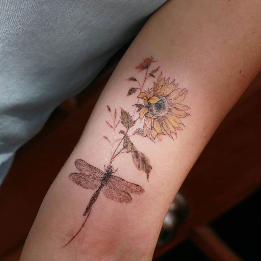Elegant dragonfly and sunflower tattoo on the forearm, featuring delicate fine-line details and soft watercolor shading for a natural look.