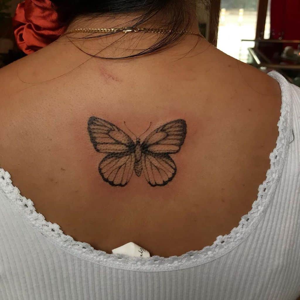 Delicate black and grey butterfly tattoo on the upper back, symbolizing transformation, freedom, and elegance.