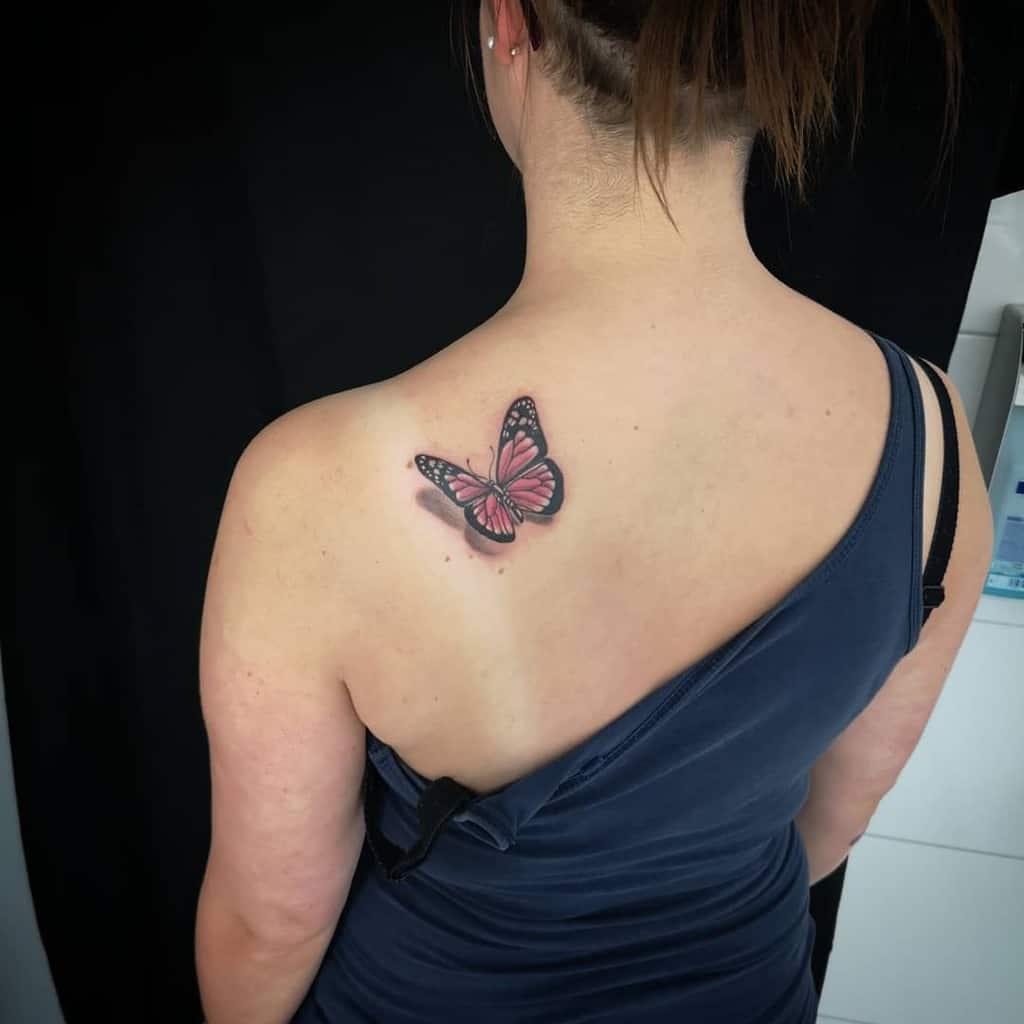 Delicate pink and black butterfly tattoo on the upper back with a subtle 3D shadow, adding an elegant and feminine touch.