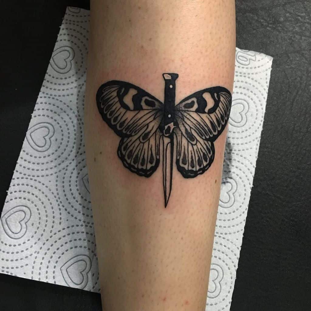 Bold black ink tattoo of a butterfly with a dagger forming its body, blending sharp and delicate elements for a striking design.