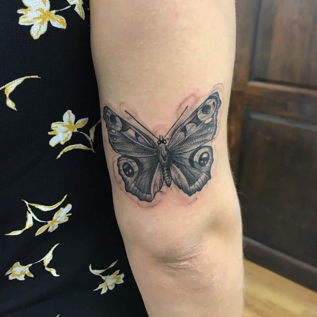 Realistic black and gray butterfly tattoo on the back of the arm, featuring intricate shading and detailed wing patterns.