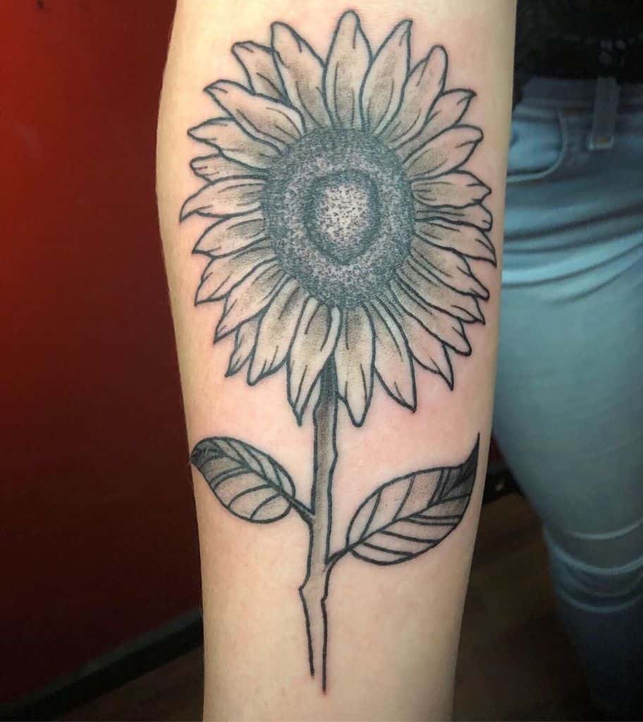 Large black and grey sunflower tattoo on forearm with bold outlines, fine shading, and detailed petals and leaves for a striking design.