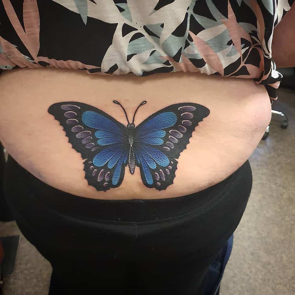 Large blue and black butterfly tattoo on the lower back, featuring bold shading and intricate wing details for a striking design.