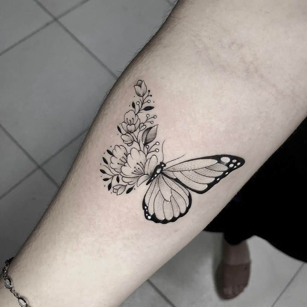 Delicate black and grey butterfly and floral tattoo on the forearm, blending soft shading with intricate linework for an elegant look.