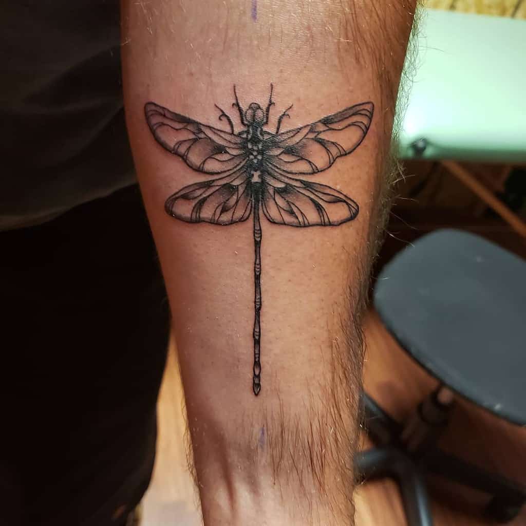 Detailed black ink dragonfly tattoo on the forearm, featuring fine linework and subtle shading for a realistic effect.