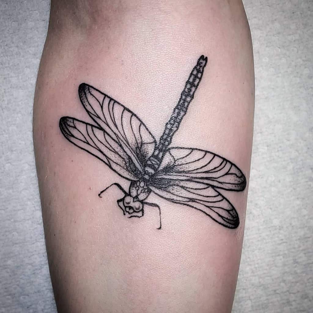 Black ink dragonfly tattoo with fine linework and intricate wing details, placed on the leg for a bold yet delicate look.