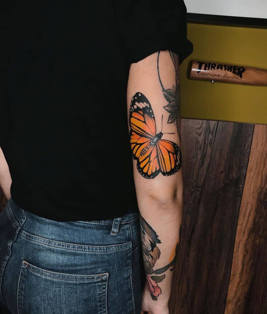 Bold orange and black monarch butterfly tattoo on the upper arm, featuring intricate wing details and a realistic design.
