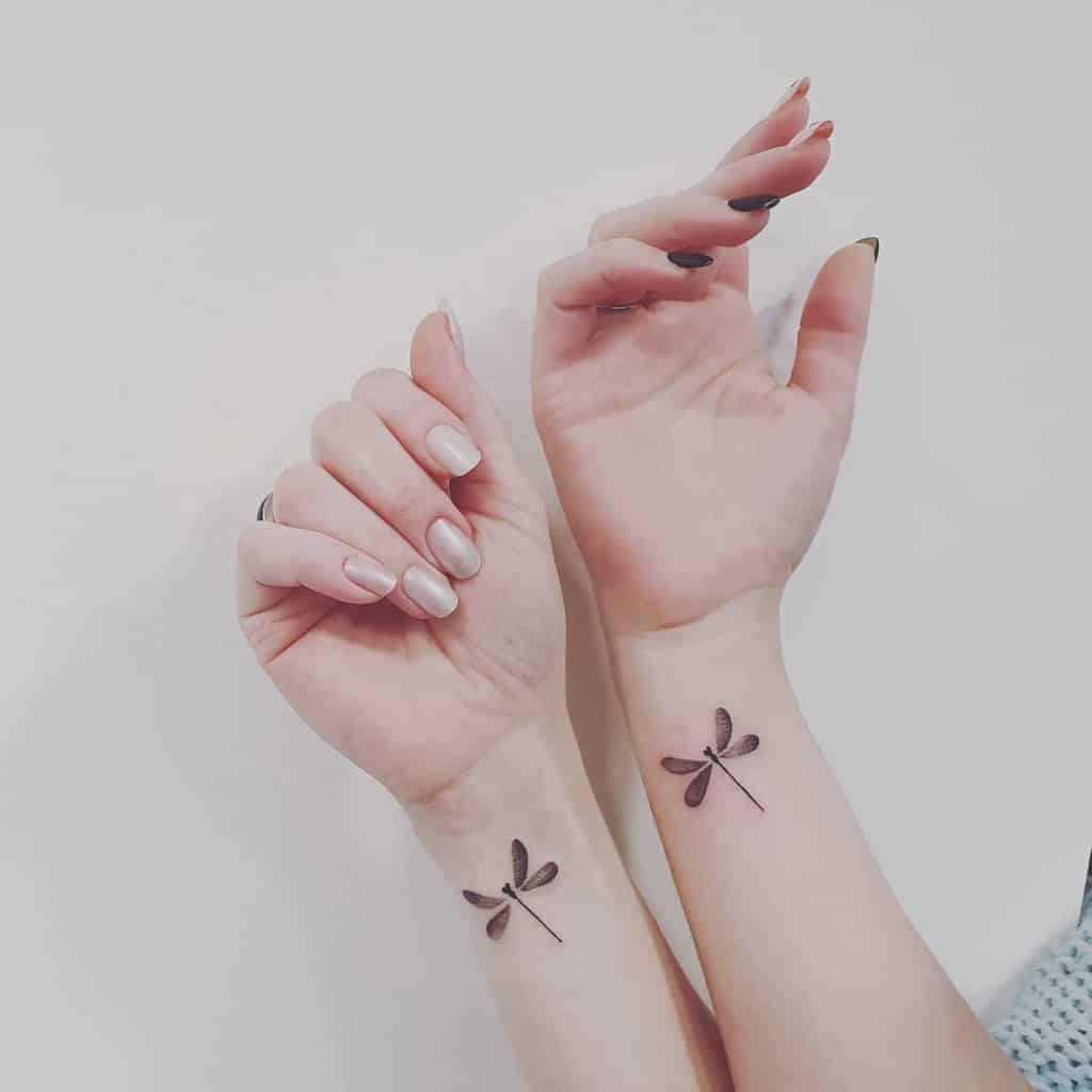 Minimalist matching dragonfly tattoos on both wrists. The simple black ink design features delicate wings and a sleek, modern look.