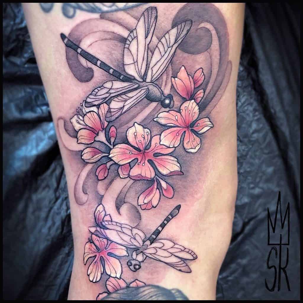 Vibrant dragonfly and cherry blossom tattoo with bold black outlines, soft pink flowers, and swirling details for a dynamic, artistic look.