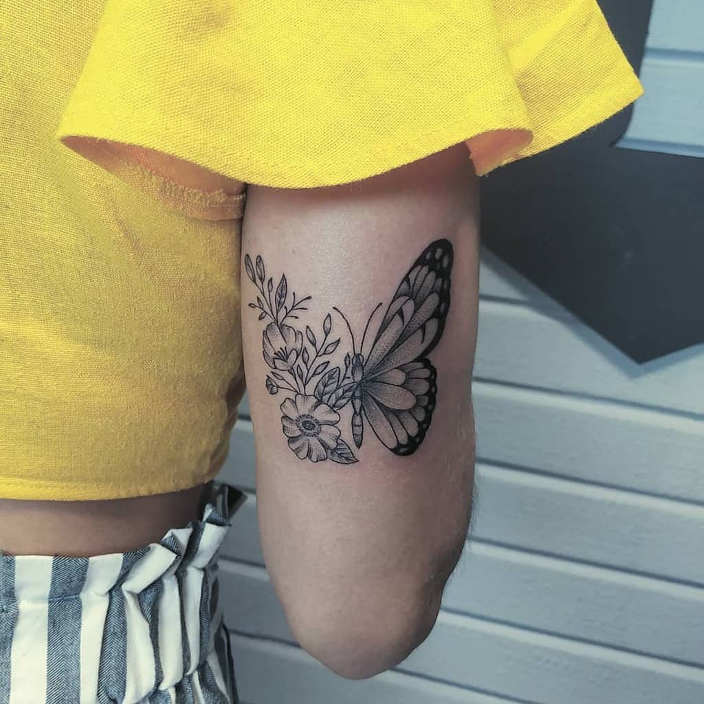 Elegant black and grey butterfly tattoo on the upper arm, featuring a floral wing design symbolizing growth and transformation.