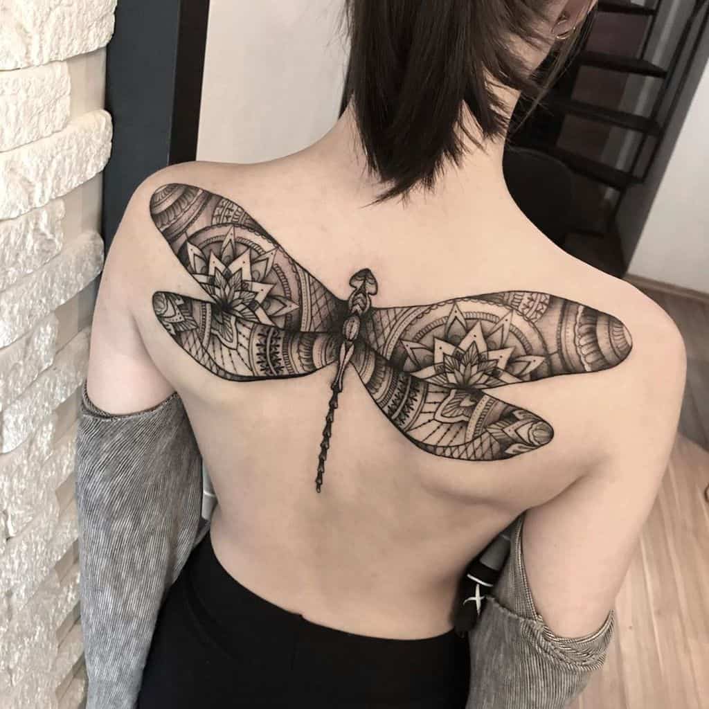 Large mandala-style dragonfly tattoo on the upper back with intricate geometric patterns and bold black ink shading.