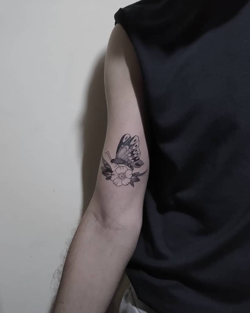 Minimalist black and grey butterfly and floral tattoo on the upper arm, combining delicate details with a subtle and elegant design.