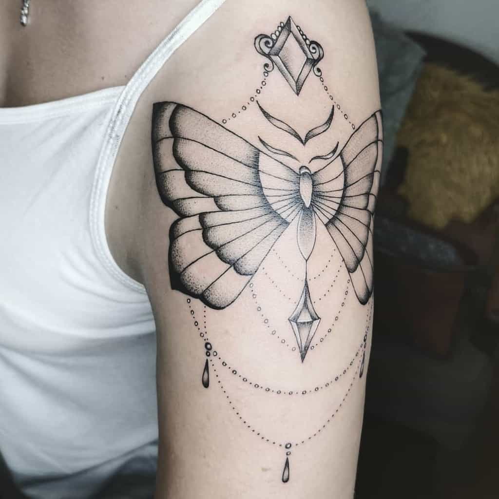 Elegant black ink butterfly tattoo on the upper arm, featuring geometric details, fine dotwork, and ornamental jewelry-like accents.