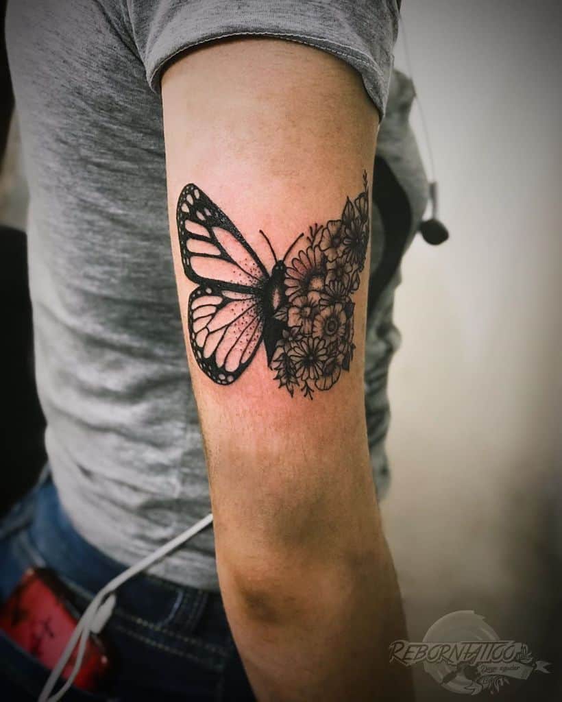 Black and grey butterfly tattoo with one wing transforming into detailed flowers, symbolizing growth and transformation on the upper arm.