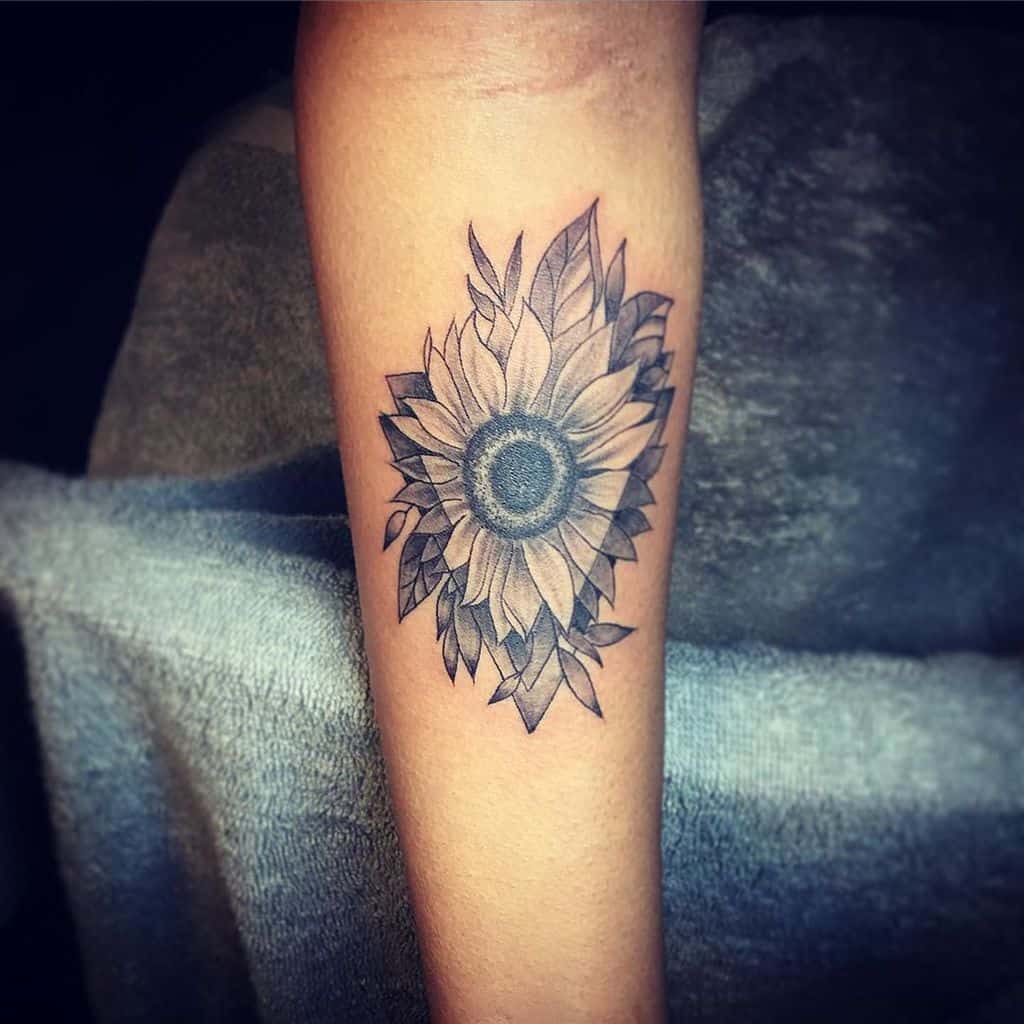 Black and grey sunflower tattoo on forearm with intricate shading, fine line details, and layered leaves for a bold floral design.