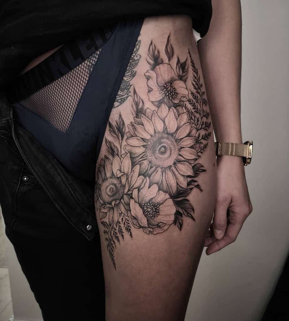 Large black and grey thigh tattoo featuring detailed sunflowers, poppies, and foliage with intricate shading for a bold floral design.