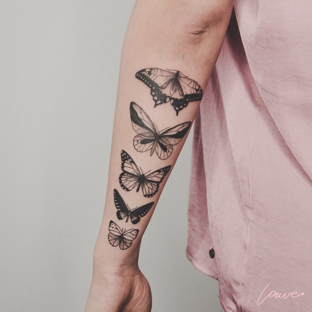 Black and gray forearm tattoo featuring five butterflies in a vertical arrangement, each with unique shading and wing details.
