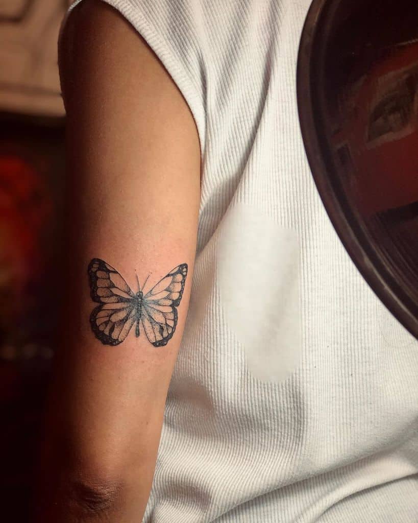 Delicate black and gray butterfly tattoo on the upper arm, featuring fine shading and intricate wing details for a soft, elegant look.