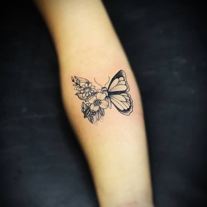 Delicate black and grey butterfly tattoo with one wing transforming into intricate flowers, symbolizing growth and transformation.