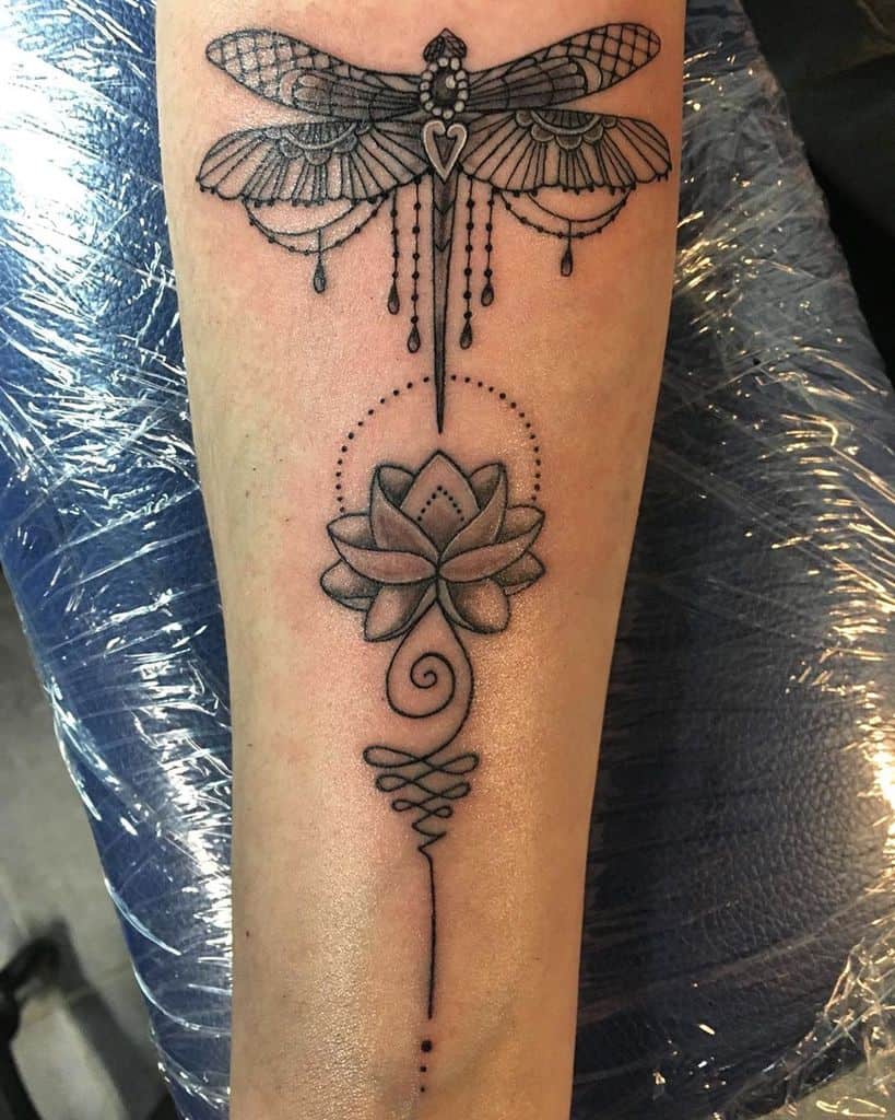 Elegant dragonfly and lotus tattoo on the forearm, featuring fine linework, ornamental details, and dot shading for a mystical design.