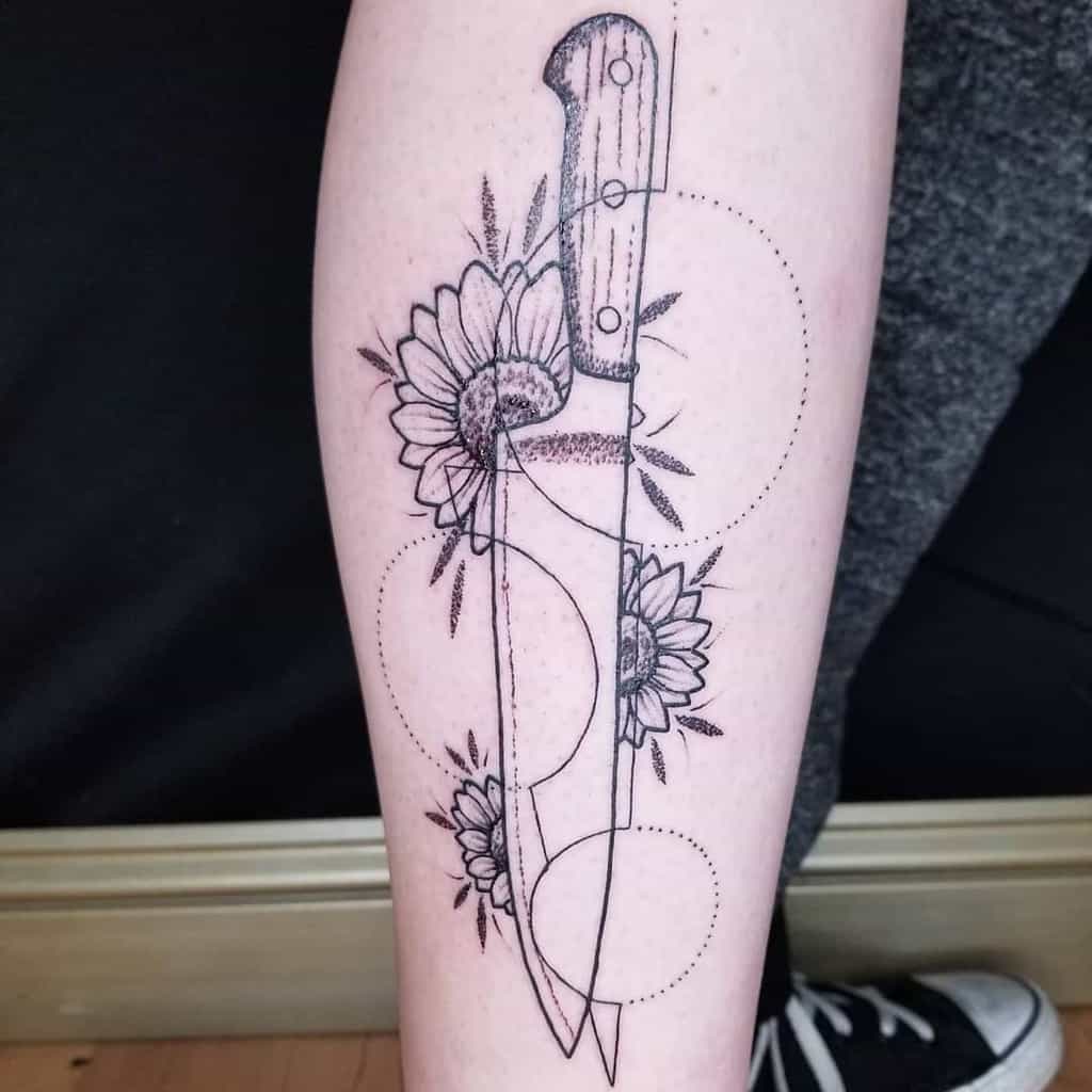 Black ink tattoo featuring a large knife with detailed sunflowers growing around the blade, accented with geometric dotted circles.