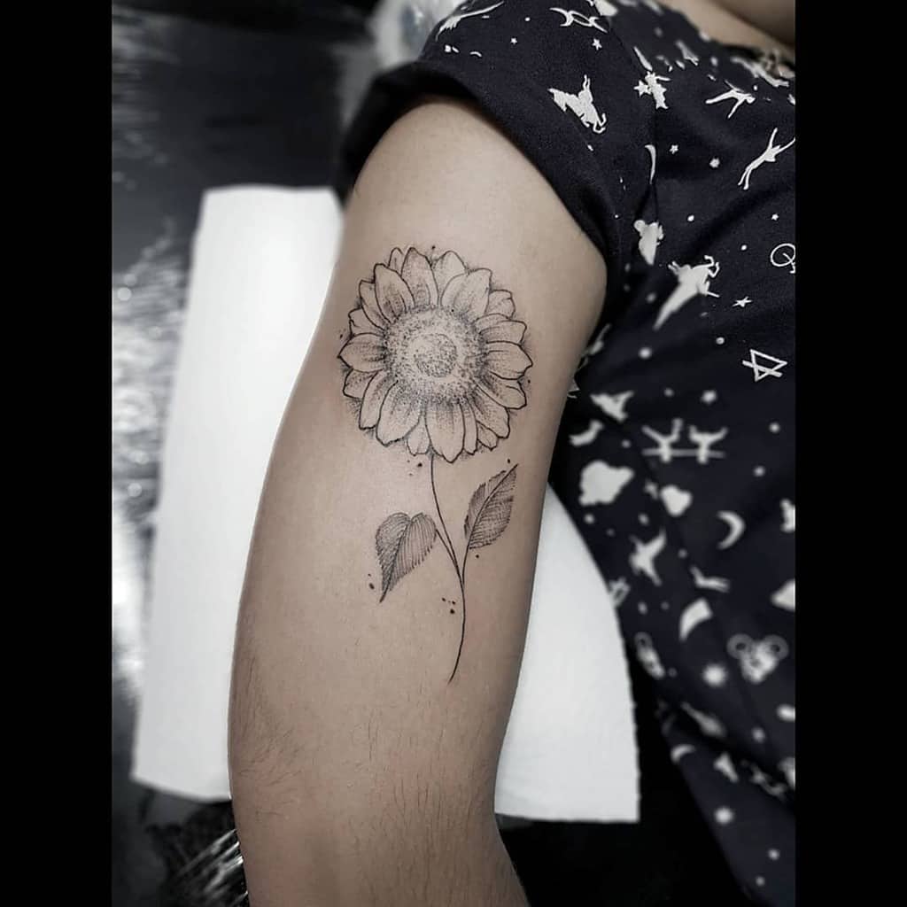 Fine line sunflower tattoo on upper arm with delicate shading, a thin curved stem, and heart-shaped leaves for a soft, elegant look.