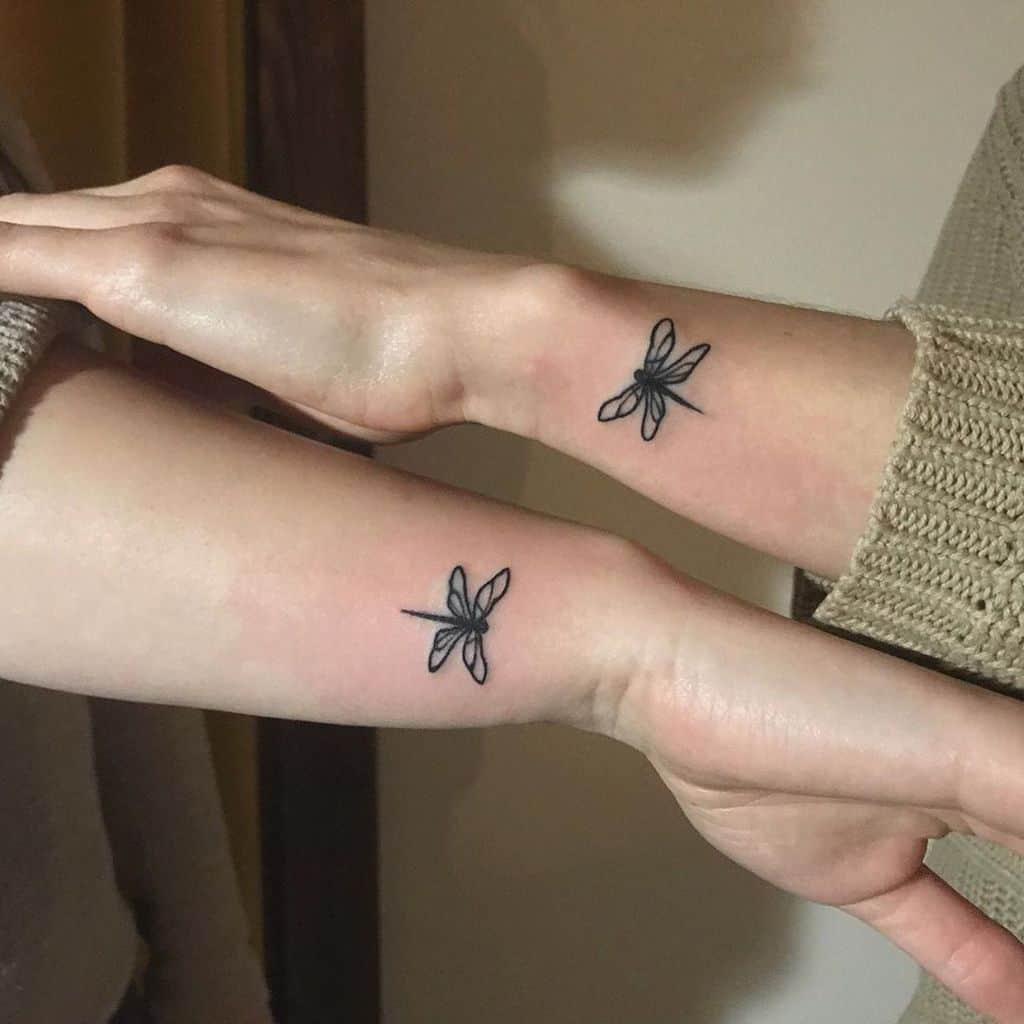 Matching minimalist dragonfly tattoos on the wrists, symbolizing connection and friendship with fine black ink linework.