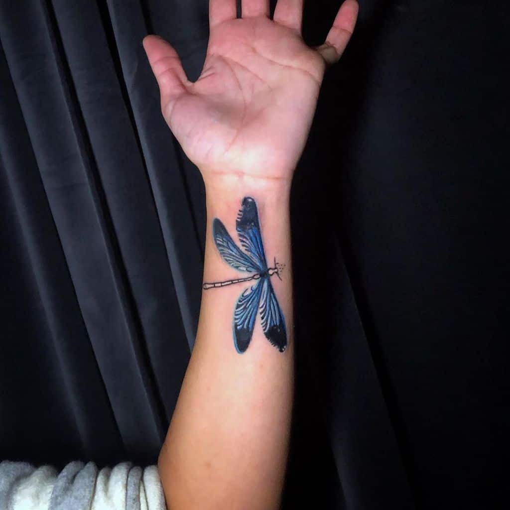 Elegant blue dragonfly tattoo on the wrist with fine details and a realistic wing design for a striking look.
