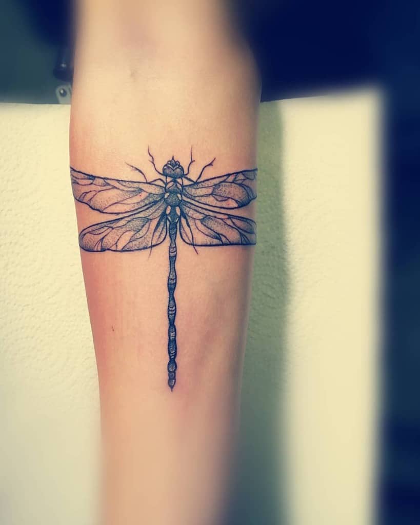 Intricate black ink dragonfly tattoo wrapped around the forearm, featuring fine linework and detailed wings for a bold design.