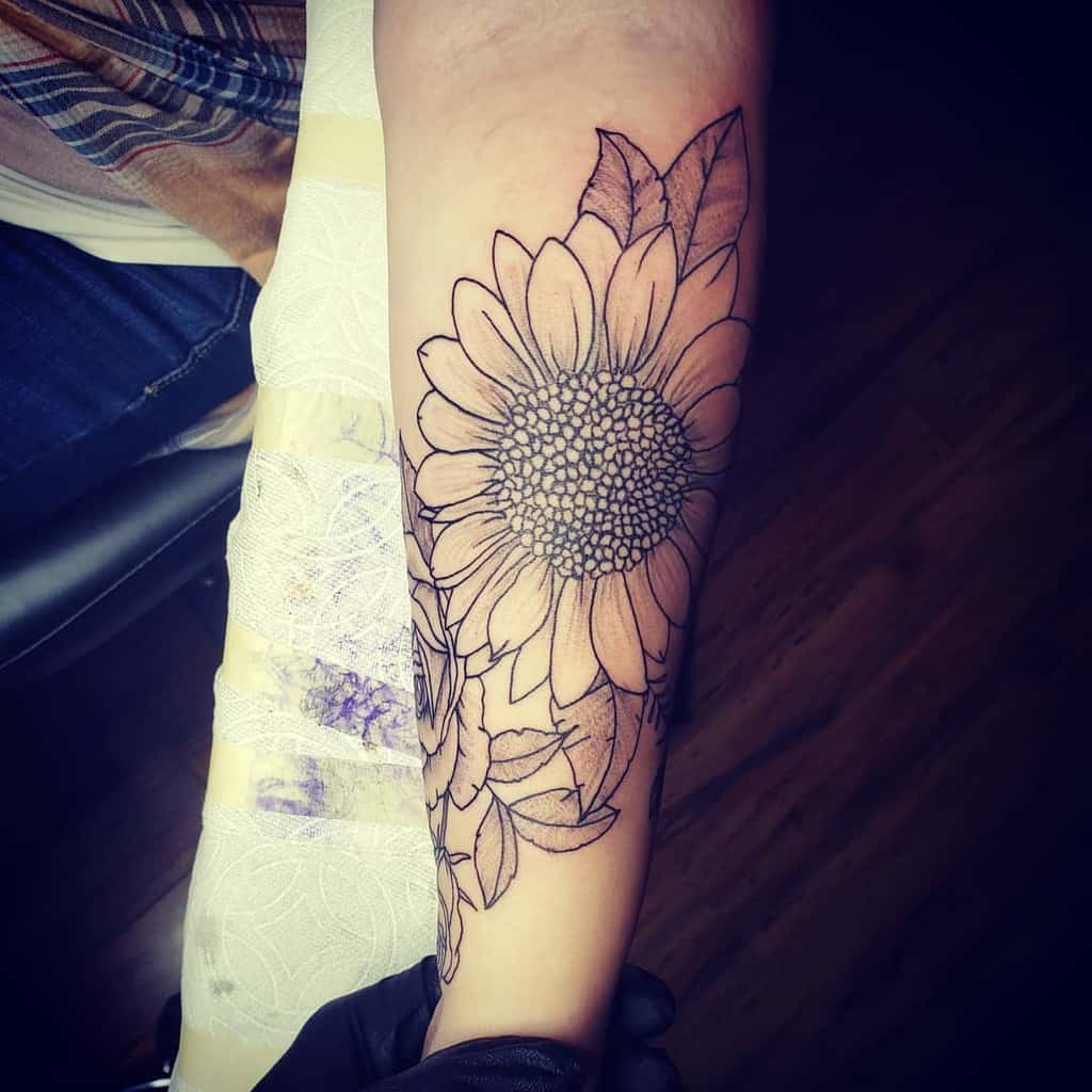 Large black ink sunflower tattoo on forearm with intricate line work and bold petal details, creating a striking floral design.