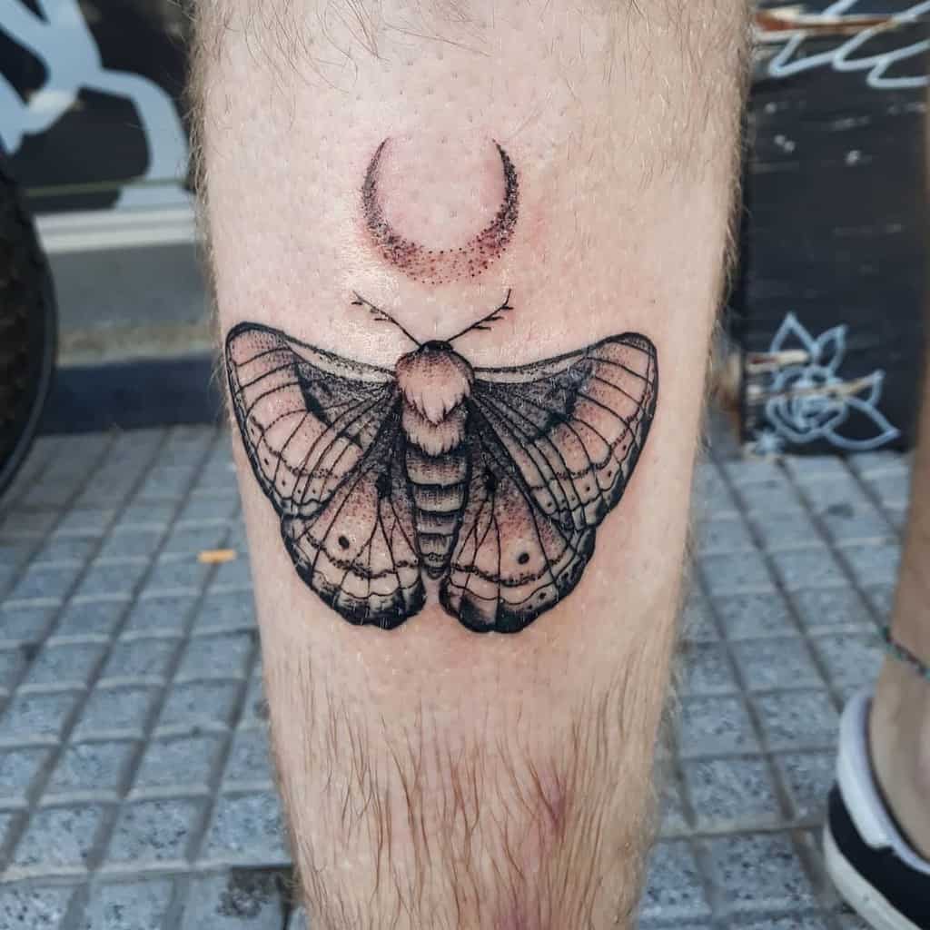 Black and gray moth tattoo on the leg, featuring intricate shading, fine details, and a crescent moon above for a mystical design.