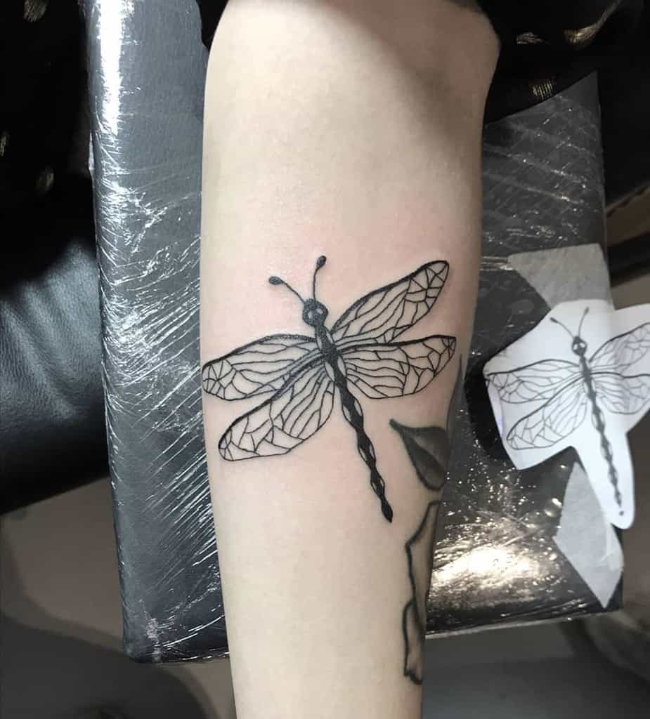 Black ink dragonfly tattoo on the forearm with geometric wing details and a bold, textured body design.